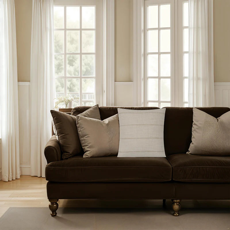 The beige Beckett woven stripe throw pillow styled on a plush dark brown velvet sofa next to neutral accent cushions.