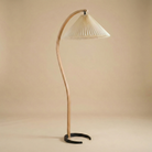 Bianca wooden floor lamp featuring a sculptural curved oak stem and a cream pleated fabric shade for a modern Scandi look.