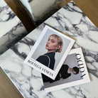 Close-up of Bulgari Charm Coffee Table in white marble with dark veining styled with fashion magazines on wooden floor