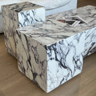 Side view of Bulgari Charm Coffee Table in white marble with dark veining, placed on wood floor beside cream sofa