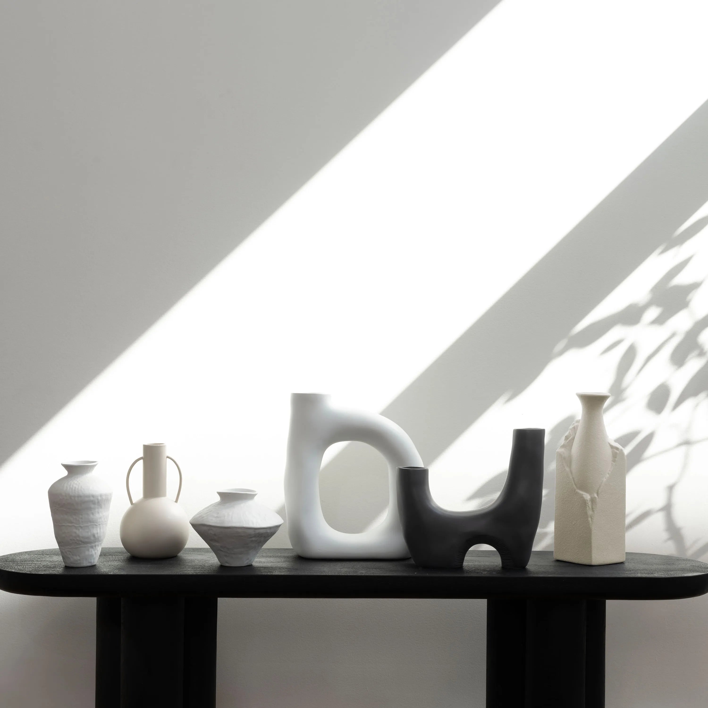 Caldera Vase in matte black styled on a console table with modern ceramic vases under natural light