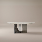 Celesti Elegance dining table featuring a round sintered stone top and sculptural stainless steel base with marble pattern accent in a neutral studio setting