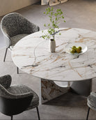 Celesti Elegance round dining table with marble-patterned sintered stone top and stainless steel base, decorated with vase and fruit bowl