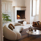 Contour Bliss Bouclé Sofa in white curved design beside fireplace and marble coffee table