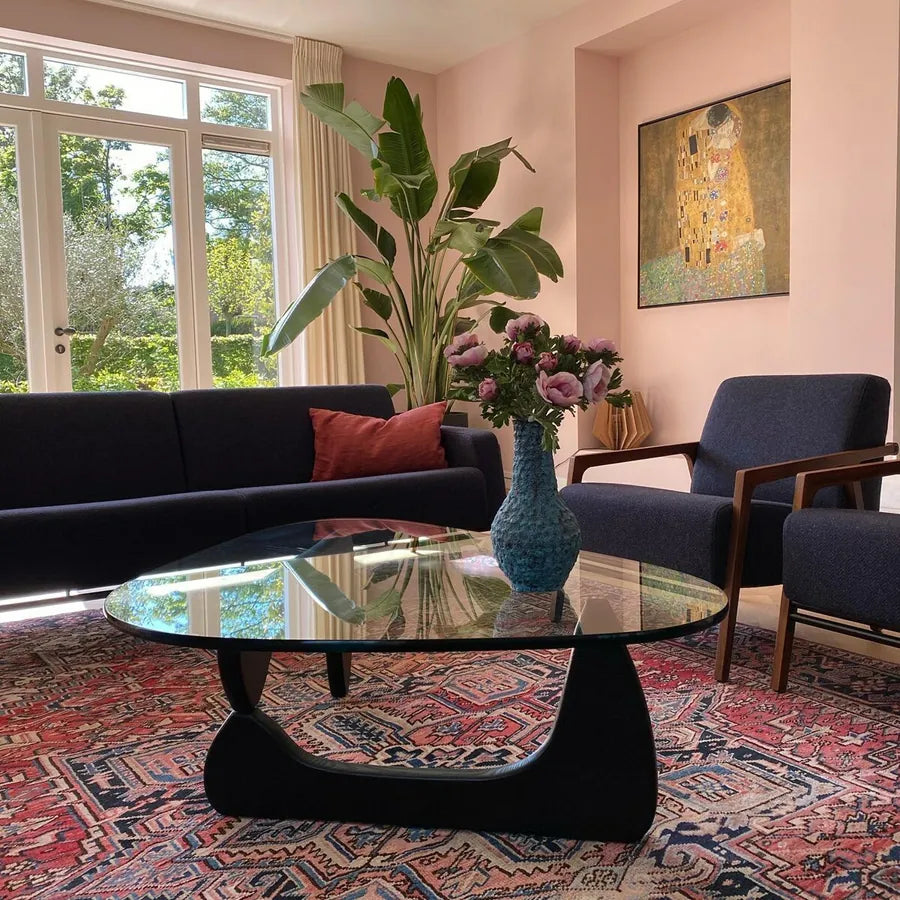 Contour Glass Coffee Table with black sculptural base and glass top styled with flowers in a bright colorful living room