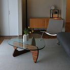 Contour Glass Coffee Table with walnut wood base and curved glass top in a minimalist living room setup
