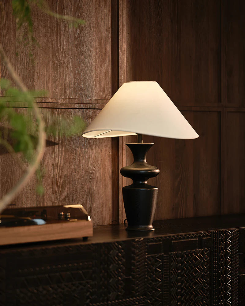 "Contour Table Lamp with black sculpted base and white shade on dark cabinet against wood-paneled wall