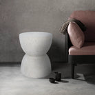 Dune textured stone side table styled next to a mauve armchair in a modern industrial living room with concrete walls.