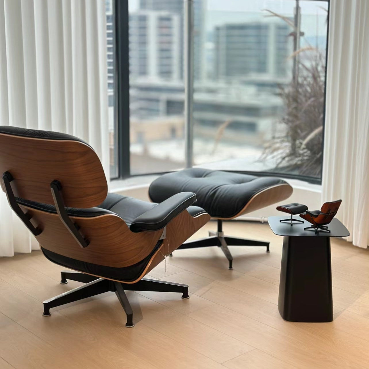 Eames Lounge Chair and ottoman in black leather with walnut shell by large window in modern apartment