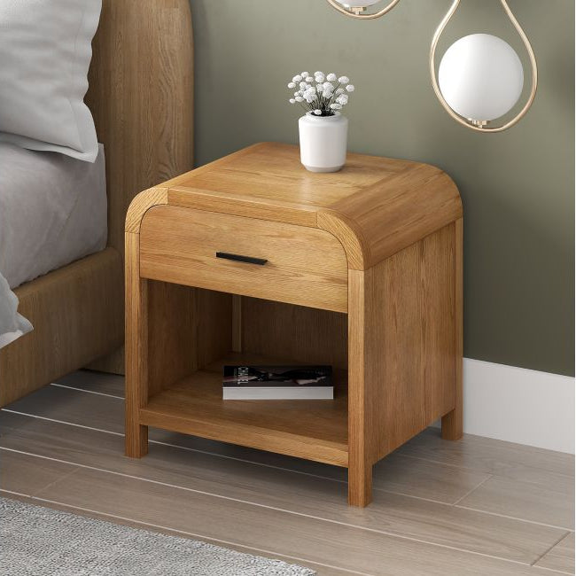 The Eamon natural light oak finished nightstand styled next to a wooden bed with a small white vase on top.