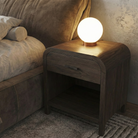 Wooden nightstand with a lit lamp next to a bed in a bedroom setting