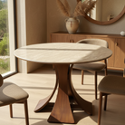 Elowen Round Dining Table with walnut base in sunlit dining room, paired with fabric chairs and natural decor