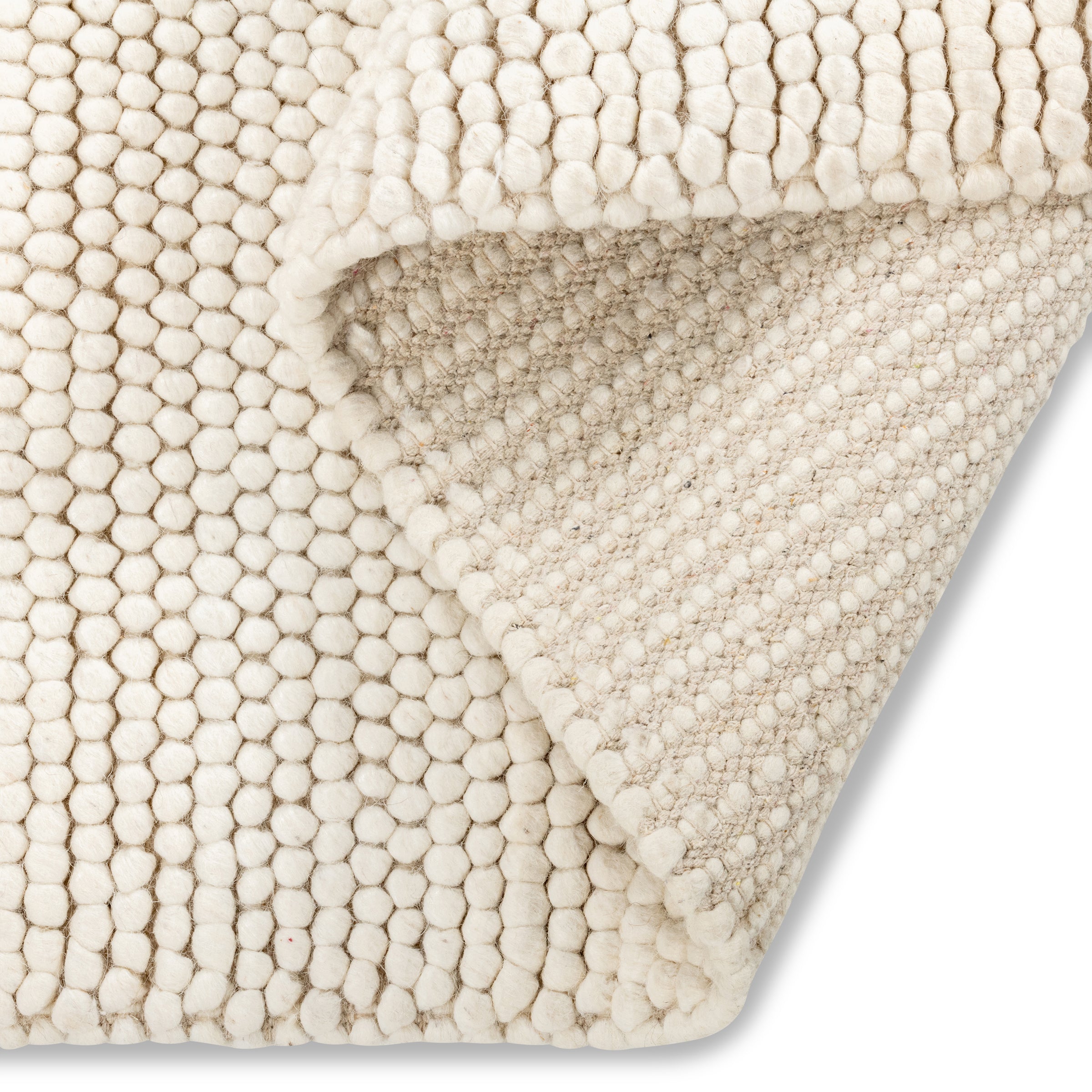 Folded corner of the cream Felix handmade textured rug, revealing its chunky pebble-like surface and sturdy backing.