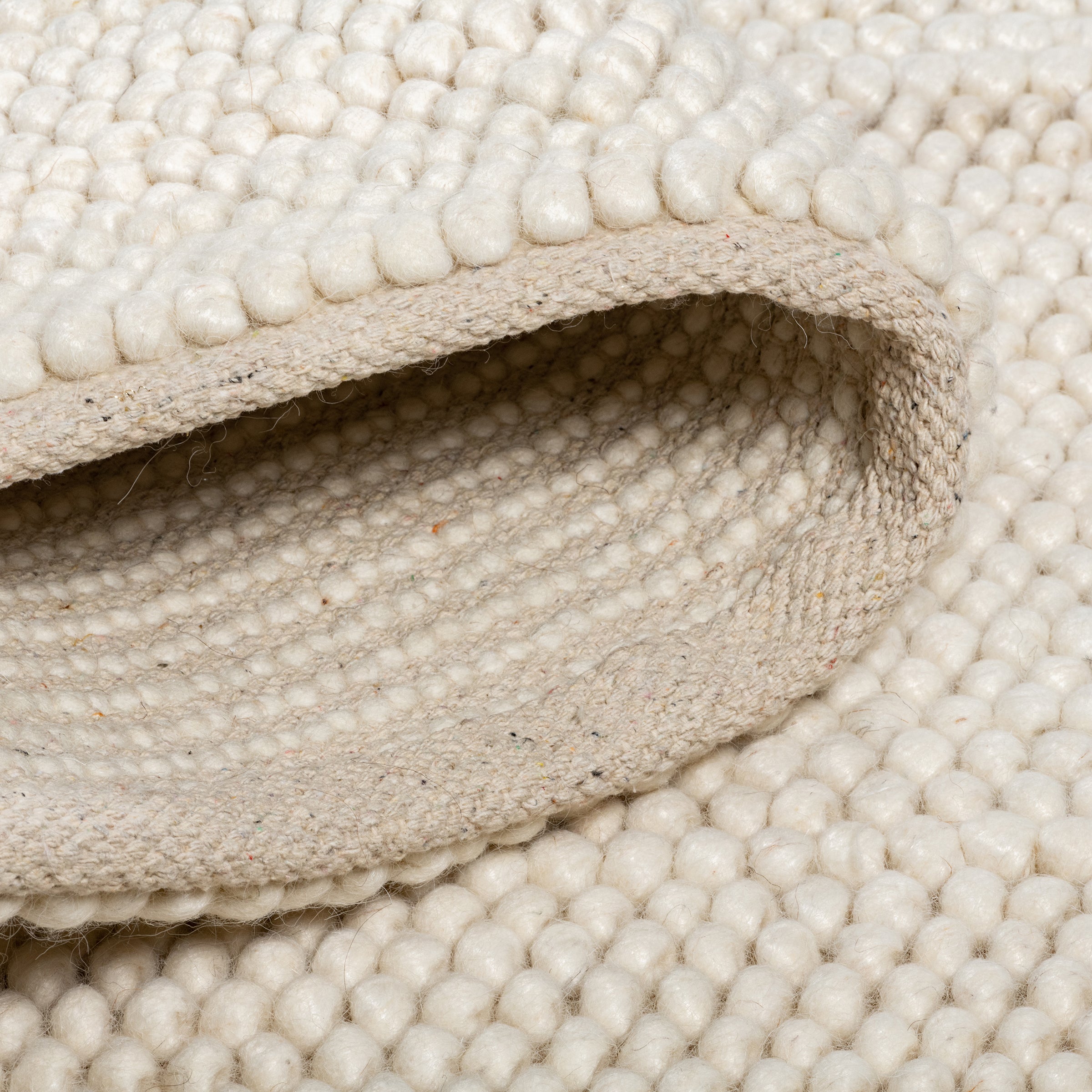 Close-up of the folded cream Felix handmade rug showing its thick, bobbly texture and canvas backing.