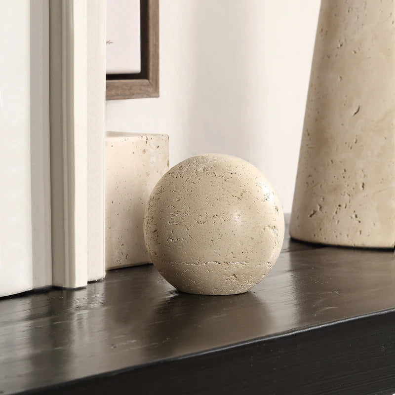 The Geo travertine stone sphere styled on a dark wooden mantel, paired with a picture frame and other natural stone decor.