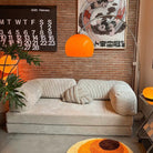 Goldenhour Adjustable Arc Floor Lamp with orange shade illuminating a cozy living room with retro art and beige sofa