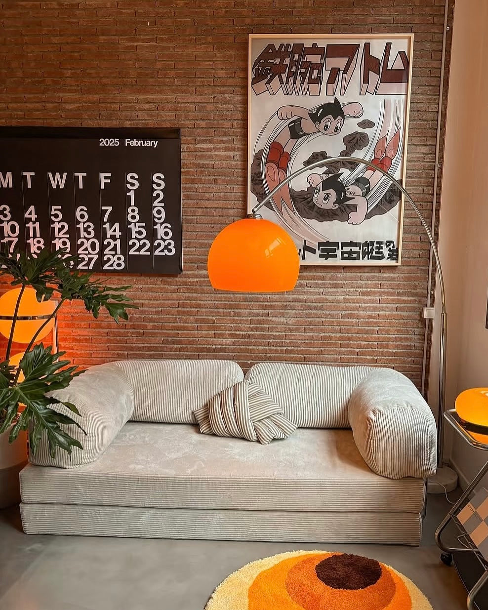 Goldenhour Adjustable Arc Floor Lamp with orange shade illuminating a cozy living room with retro art and beige sofa