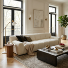 The Gummy cream bouclé sofa styled in an elegant, airy living room with a travertine coffee table, abstract art, and tall windows.
