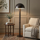 Harrison bronze floor lamp with a dome shade in a living room setting next to a beige armchair.