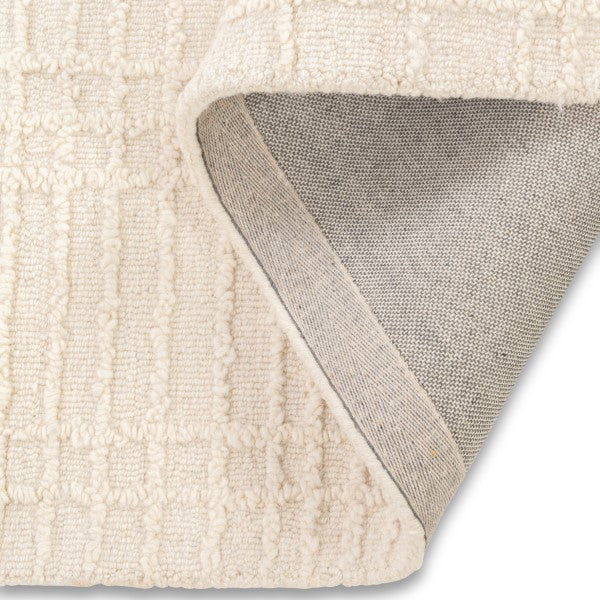 Folded corner of the neutral Hayes textured grid rug showing the underside woven backing construction.