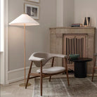 Horizon Shade Floor Lamp with brass base and wide linen shade placed beside a modern wood accent chair and marble fireplace