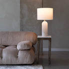 Iris Onyx Table Lamp on rustic wood side table beside a beige sofa in a modern living room with concrete wall backdrop