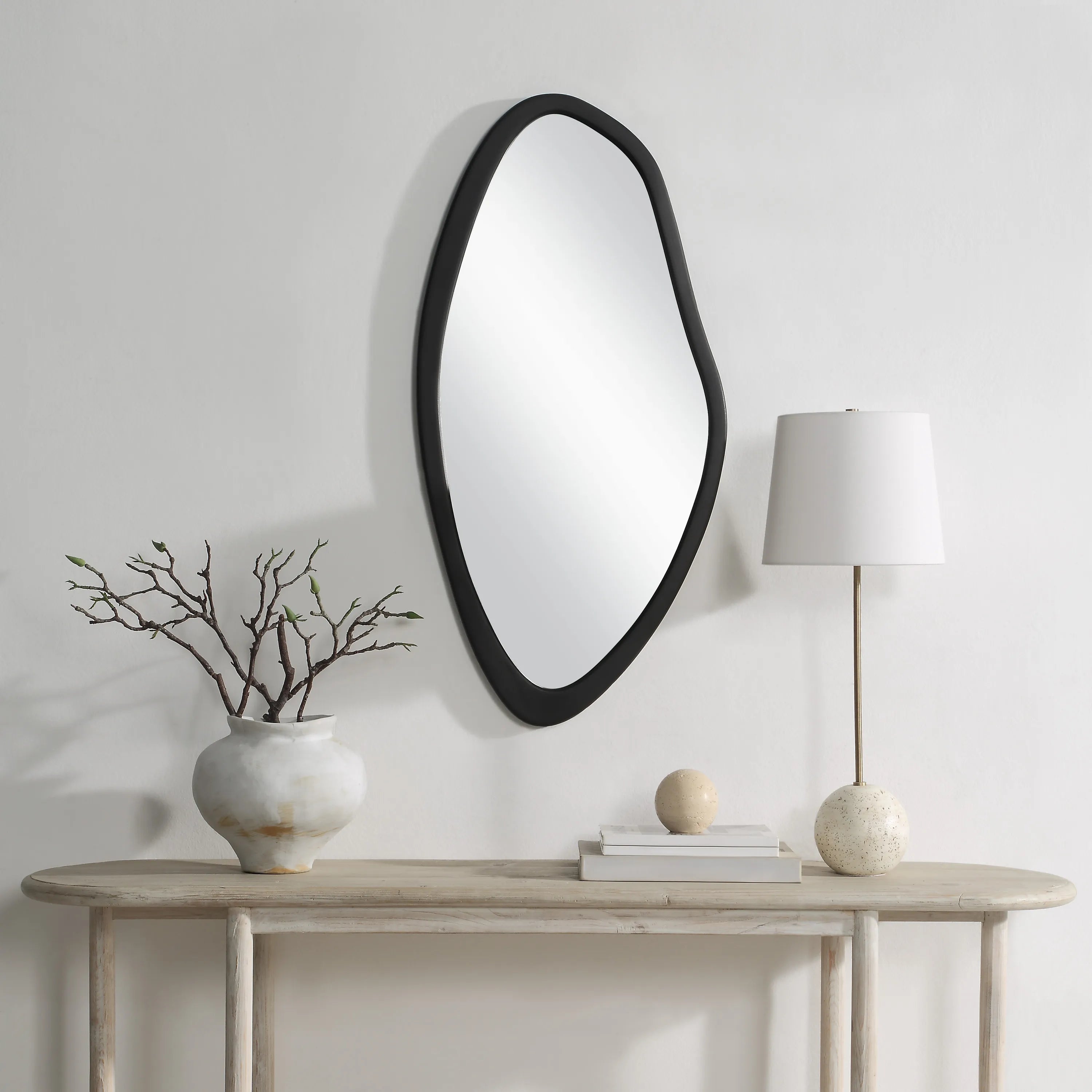 Isla Wall Mirror styled above a console table, featuring an asymmetrical black frame in a modern entryway.