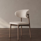 Linen Ash Wood Dining Side Chair with a curved upholstered back and ash wood frame, styled in a neutral room with dark wood flooring