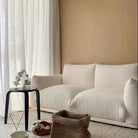 Loaf Bread Sofa in creamy boucle fabric placed in a cozy living room with beige wall, sheer curtains, and woven baskets