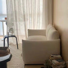 Side view of Loaf Bread Sofa in white boucle fabric beside soft beige wall, with books, curtains, and accent table nearby