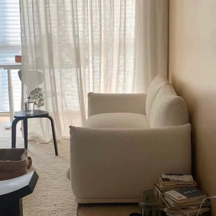 Side view of Loaf Bread Sofa in white boucle fabric beside soft beige wall, with books, curtains, and accent table nearby