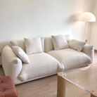 Loaf Bread Sofa in white boucle fabric with plush cushions placed in a bright living space beside a floor lamp and glass table