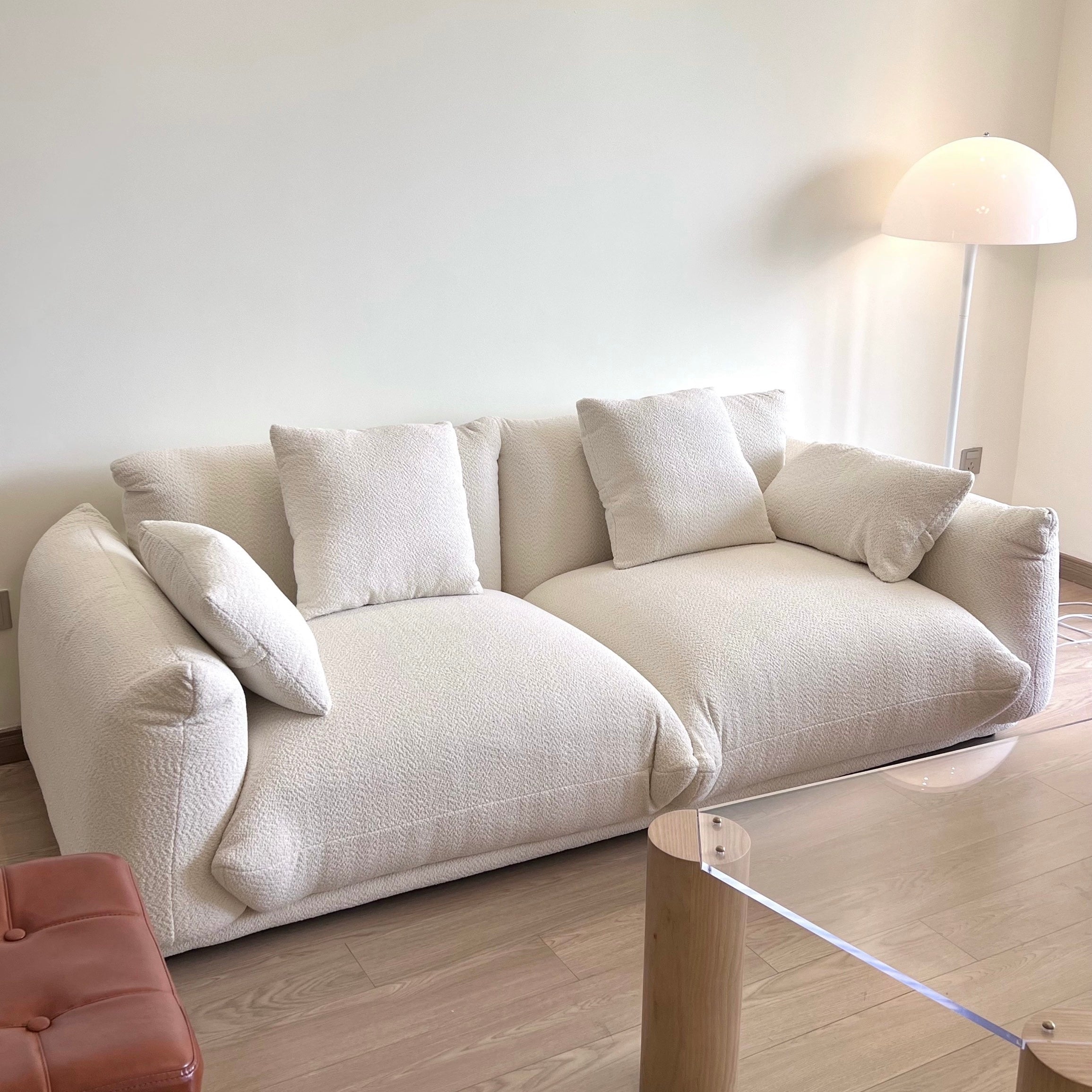Loaf Bread Sofa in white boucle fabric with plush cushions placed in a bright living space beside a floor lamp and glass table