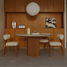 Lucia Dining Table with round sintered stone top and fluted wood base, paired with beige upholstered chairs in a modern dining space