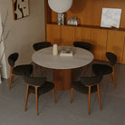 Lucia Dining Table with round sintered stone top and fluted wood base, surrounded by six dark upholstered chairs in a warm modern room