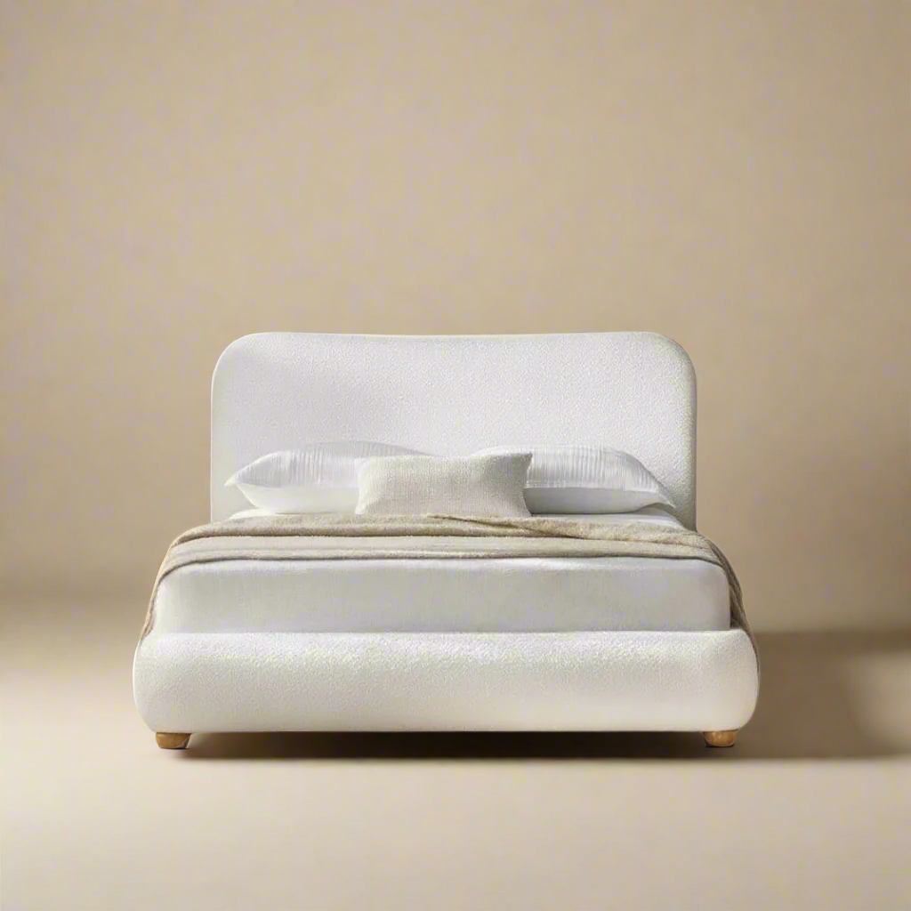 Luma Bouclé Bed in white boucle fabric with rounded frame and soft curved headboard styled in a minimal beige studio setting