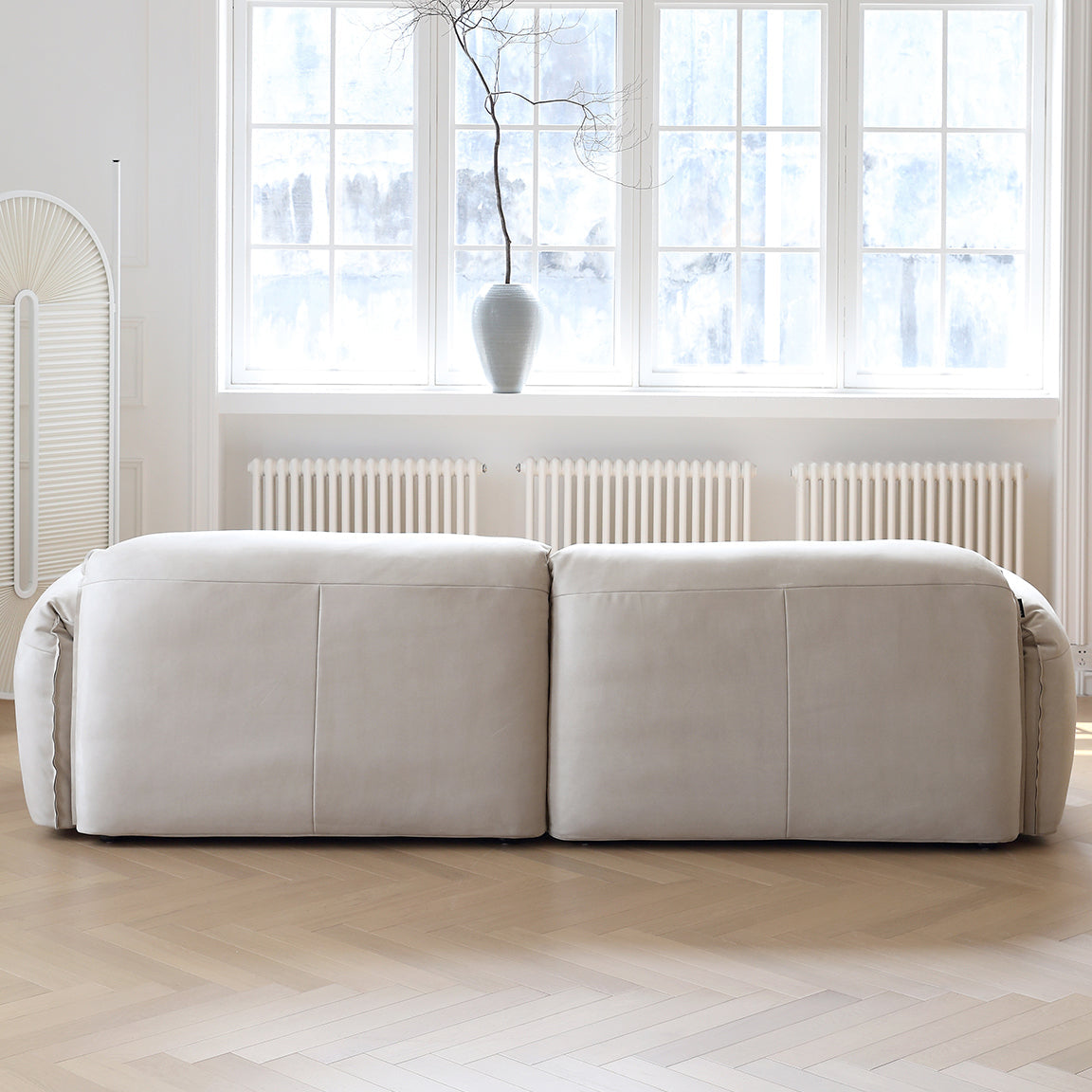 Back view of Luxury Elephant Ear Sofa in cream ultra suede with rounded edges in a bright living room with large windows
