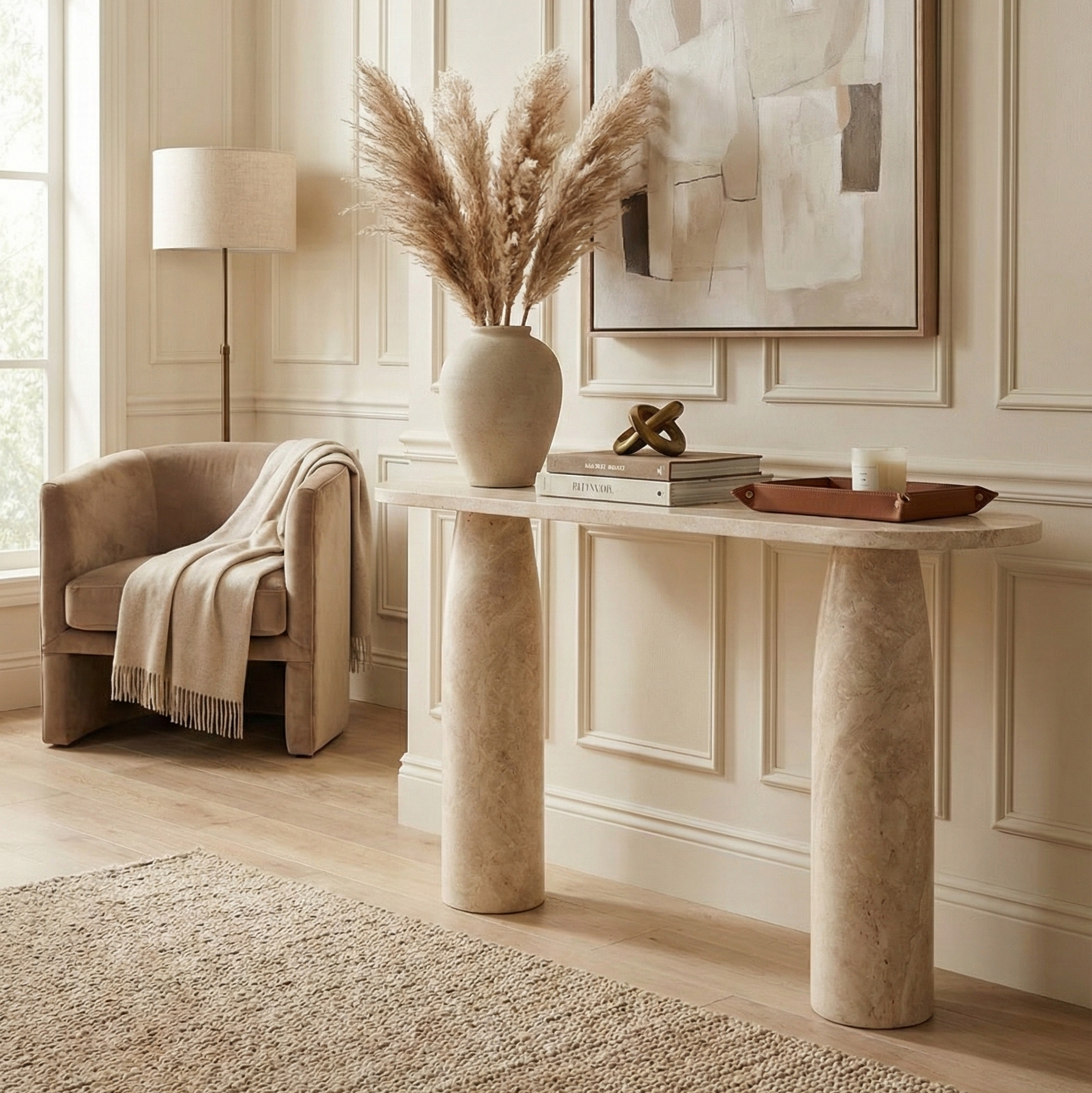 Angled view of the Maelis beige travertine console table styled in a neutral hallway with pampas grass and a velvet armchair.