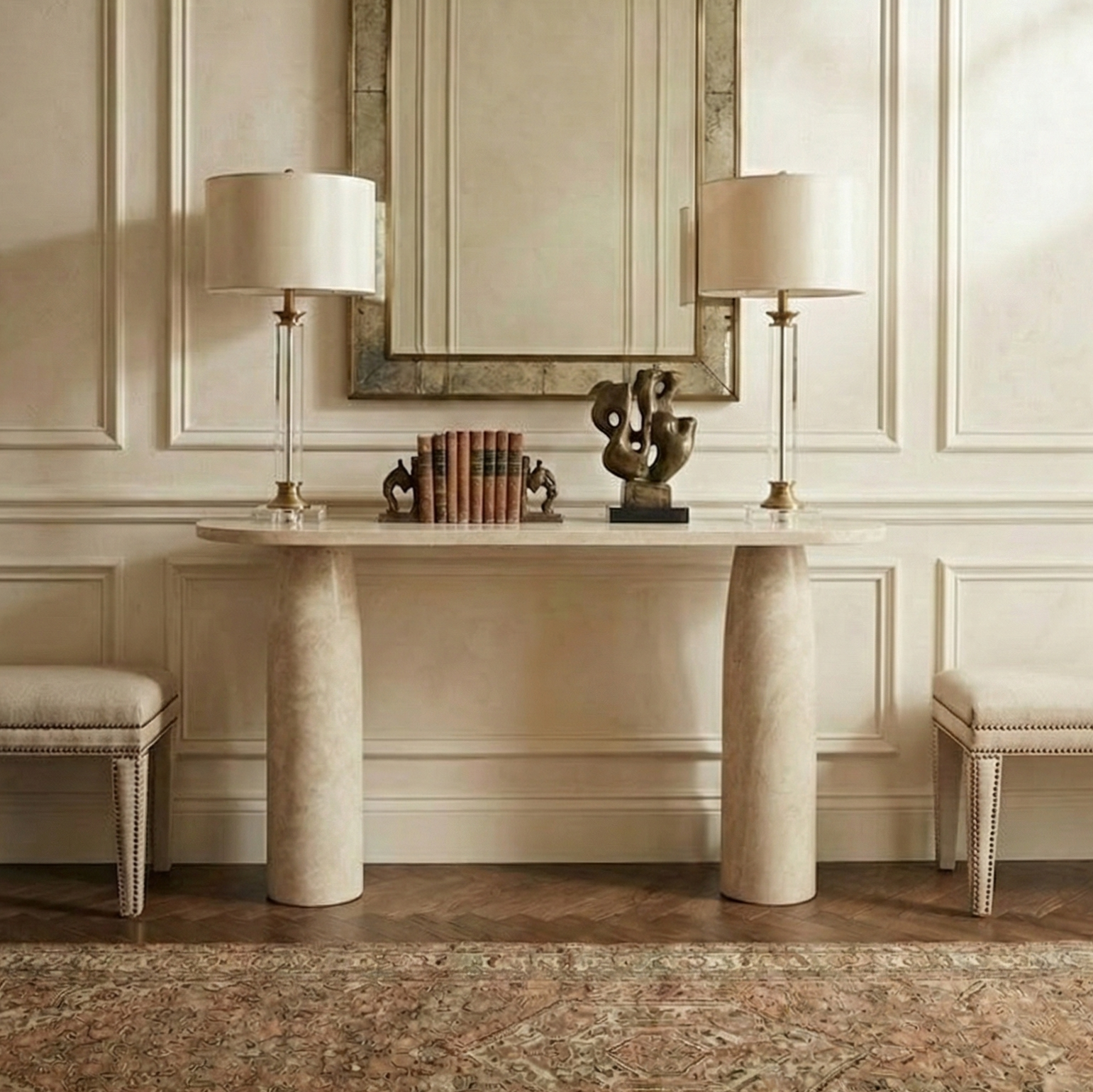 Maelis travertine stone console styled in a luxury entryway with a large wall mirror, crystal table lamps, and vintage runner rug.