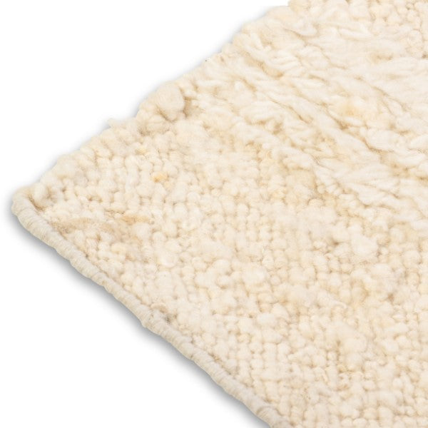 Close-up corner detail of the Maeve rug showing the neat edge binding and the contrast between the flatweave base and raised nubby wool pile.