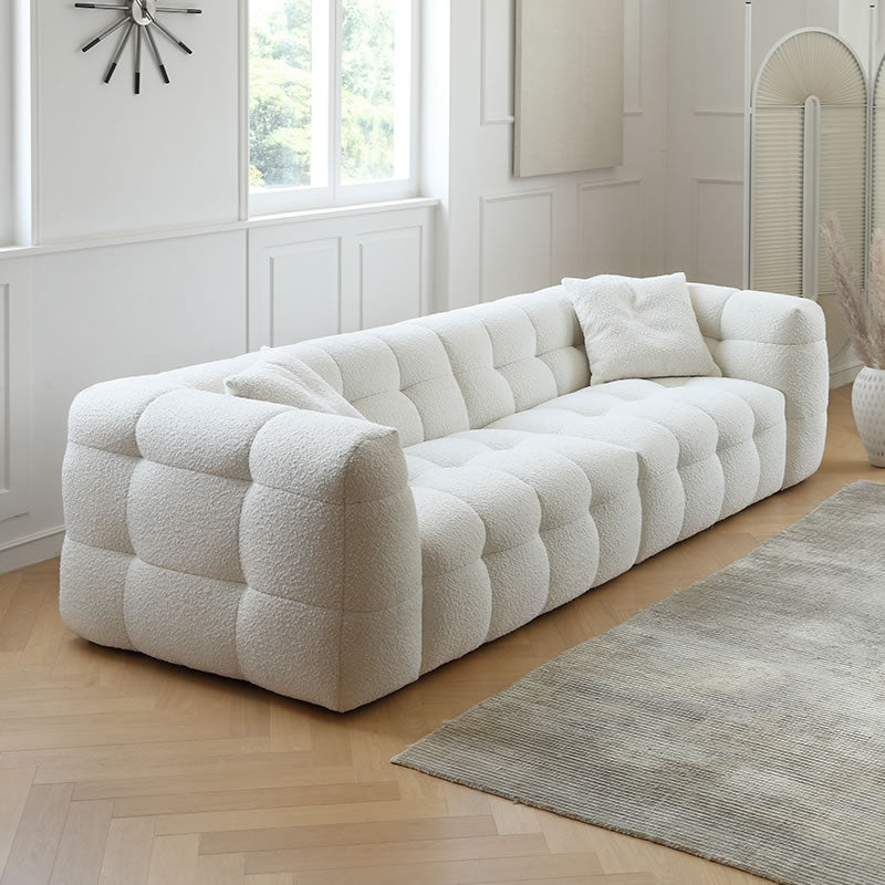 Cream bouclé modular sofa with cube tufting and pillows in a bright living room with wood floor and beige rug