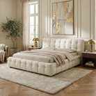 Marshmallow Puff white boucle bed styled in a bright luxury bedroom with wood floors, gold lamps, and large wall art.