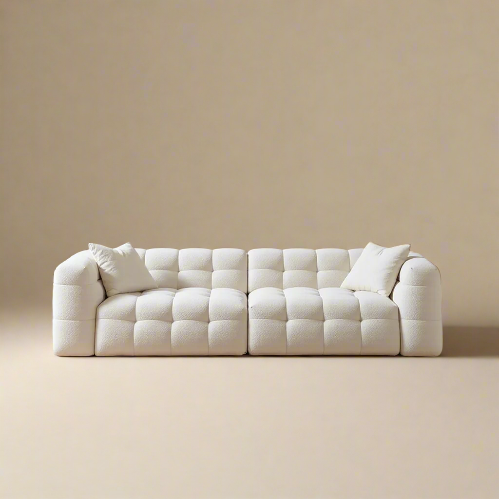 Cream bouclé modular sofa with cube tufting and rounded arms on a warm beige background with throw pillows"