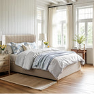 The cream Mila upholstered storage bed styled in a bright, modern bedroom with wood floors, matching nightstands, and a light blue throw blanket.