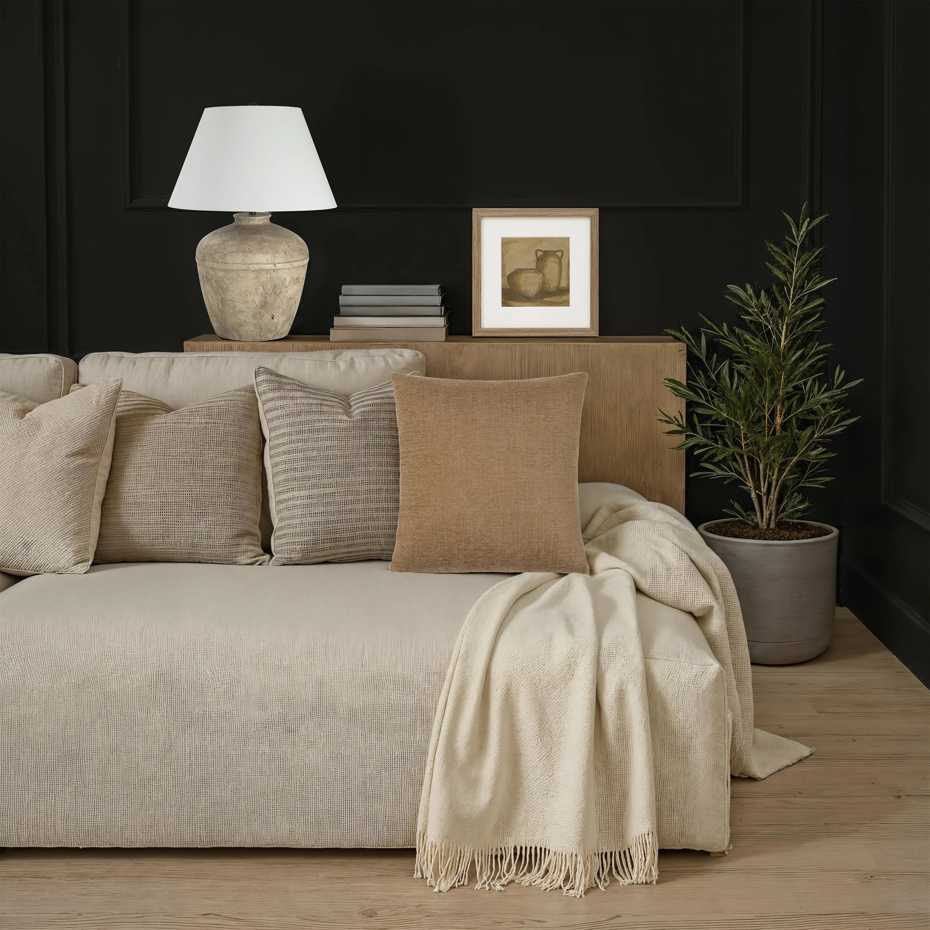 The warm camel Miles woven throw pillow styled on a light neutral sofa next to a draped blanket and an olive tree.
