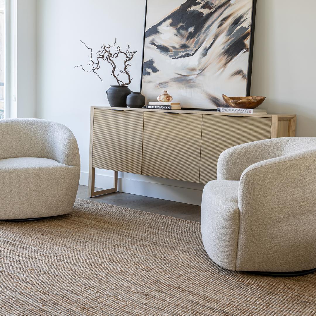 A pair of buff Milo swivel chairs styled in a bright, modern living room with a neutral jute rug and fluted wood sideboard.