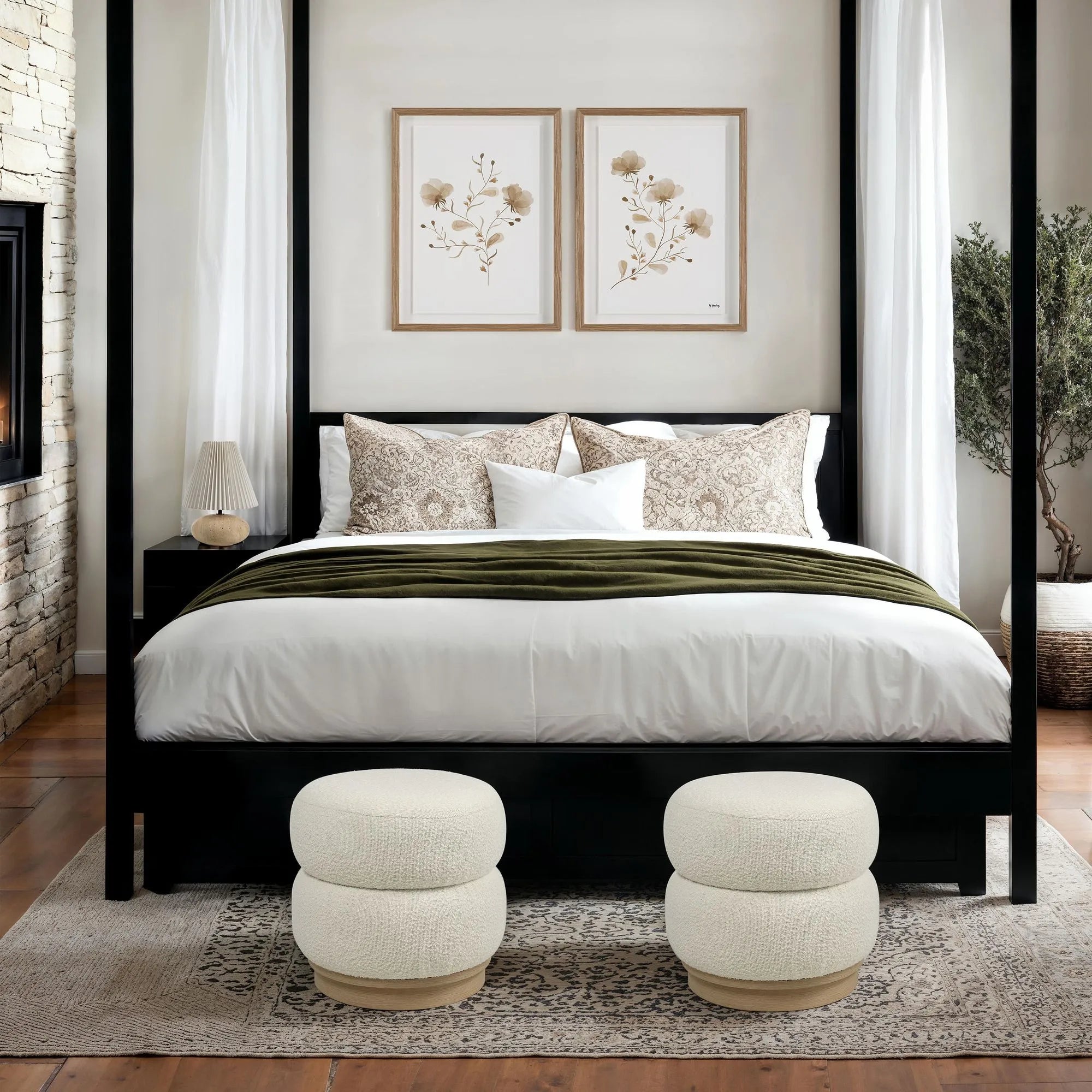 Two white Moita bouclé stools styled side-by-side at the foot of a black four-poster bed in a cozy bedroom with a stone fireplace.