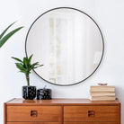 Nova Wall Mirror styled above a wooden console table with books and a plant in a bright living space