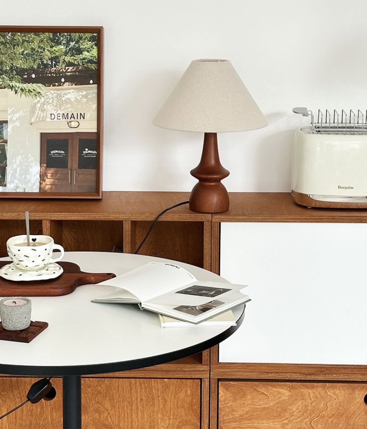 Olivia Table Lamp with walnut base placed on a wooden sideboard beside a table with cup and book