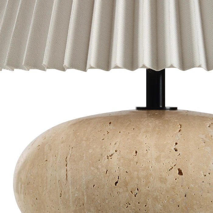 Close-up of a lamp with a pleated beige shade and textured travertine base.